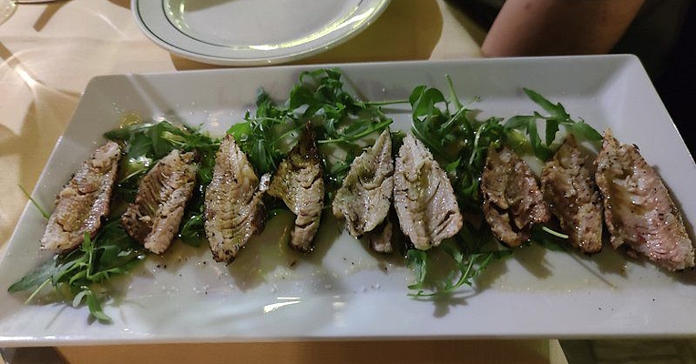 Grilled lake fish fillets served on a bed of rocket with oil and pepper, neatly arranged on a rectangular white dish.