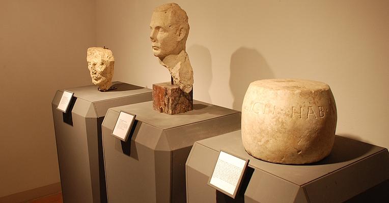 Two stone busts and a cylindrical object with Latin inscription, displayed on pedestals with labels