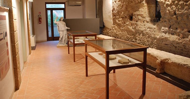 Exhibition space of an archaeological museum with display cases containing artifacts, a statue at the end of the room