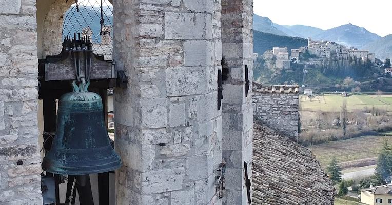 Bronze bell in a bell tower, with a medieval castle in the background