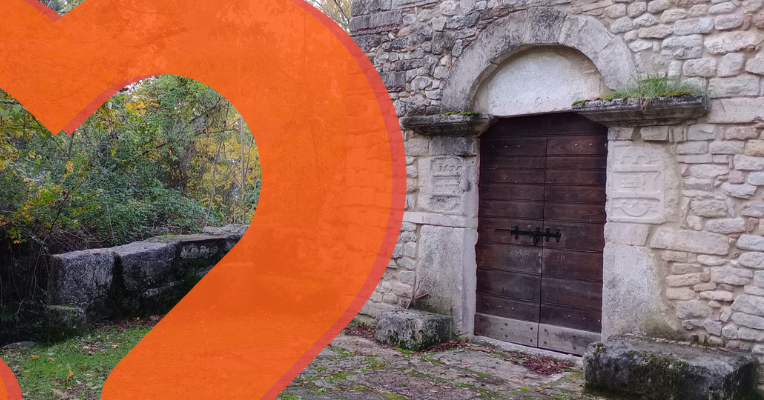 Entrance of an ancient stone building surrounded by vegetation in Cesi, with a dark wooden door framed by stone.