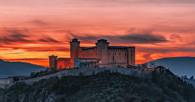 La forteresse Albornozienne dominant la ville de Spolète au coucher du soleil, illuminée par un ciel en feu