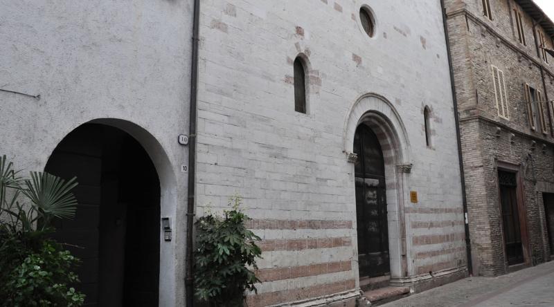 Stone façade of the Church of San Biagio in Cannara, with an arched portal and small windows, overlooking a street.
