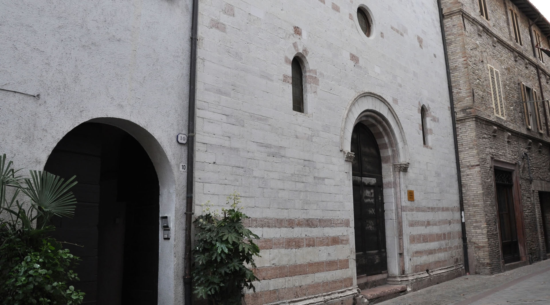 Façade en pierre de l’église San Biagio à Cannara, avec un portail en arc et de petites fenêtres, donnant sur une rue.