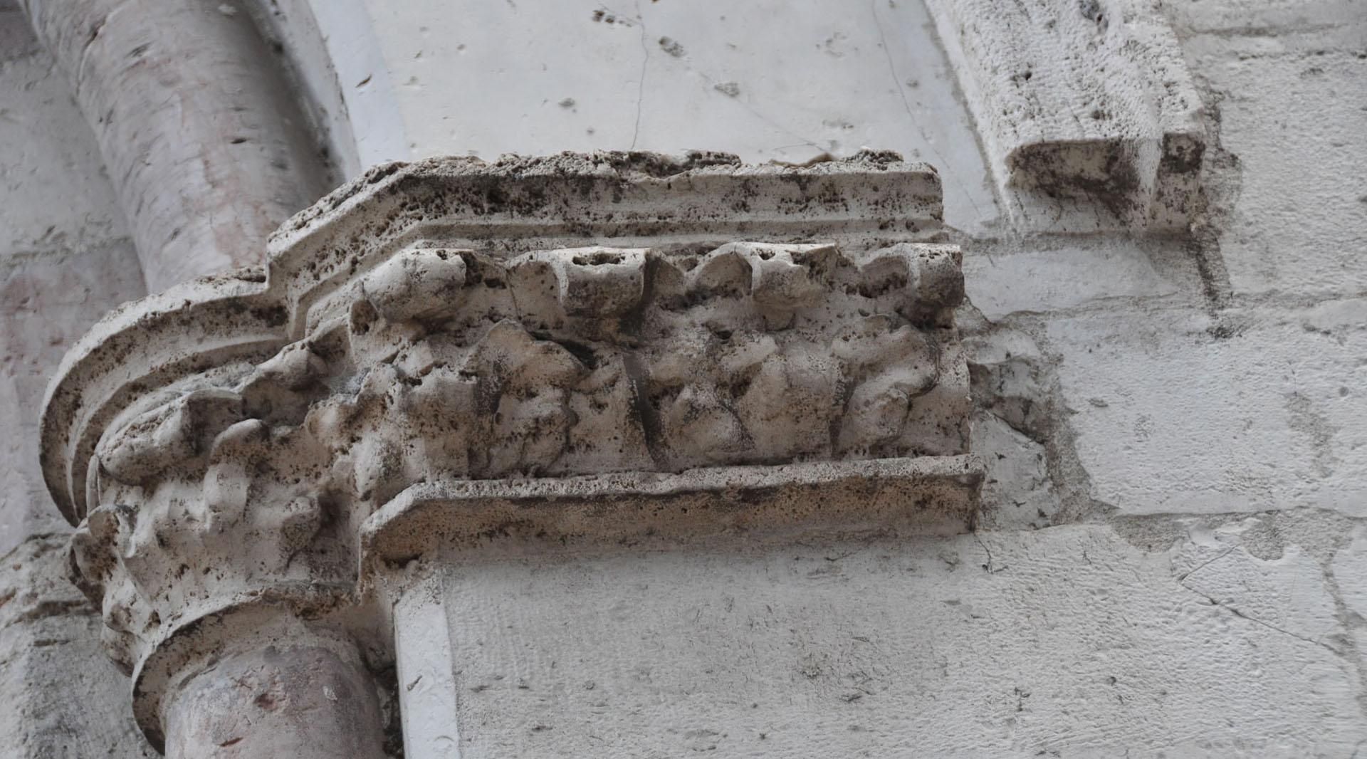 Détail d’un chapiteau sculpté en pierre, aux motifs décoratifs usés par le temps, sur la façade de l’église.