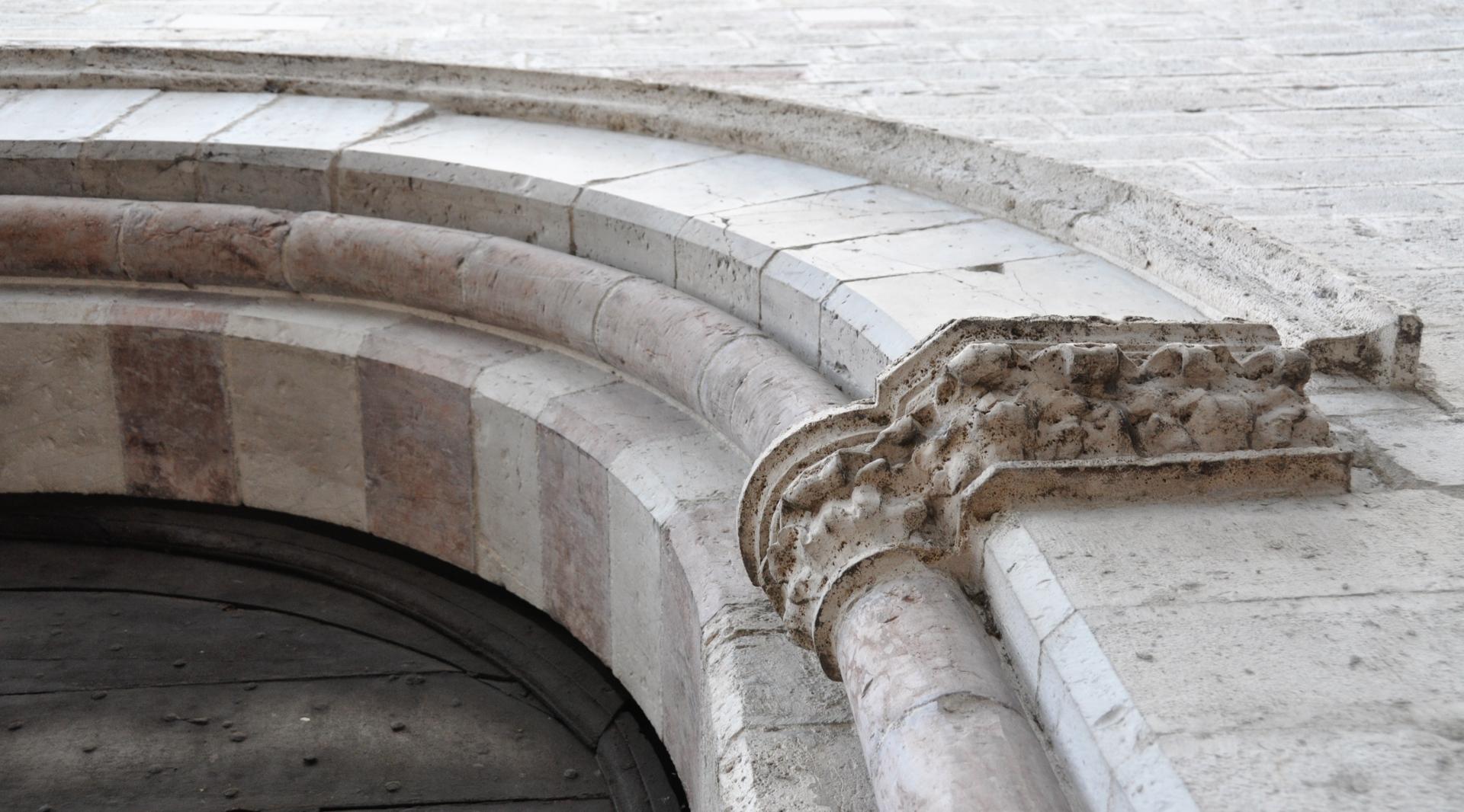 Détail du portail en arc de l’église en pierre, avec un chapiteau sculpté et des décorations usées par le temps.
