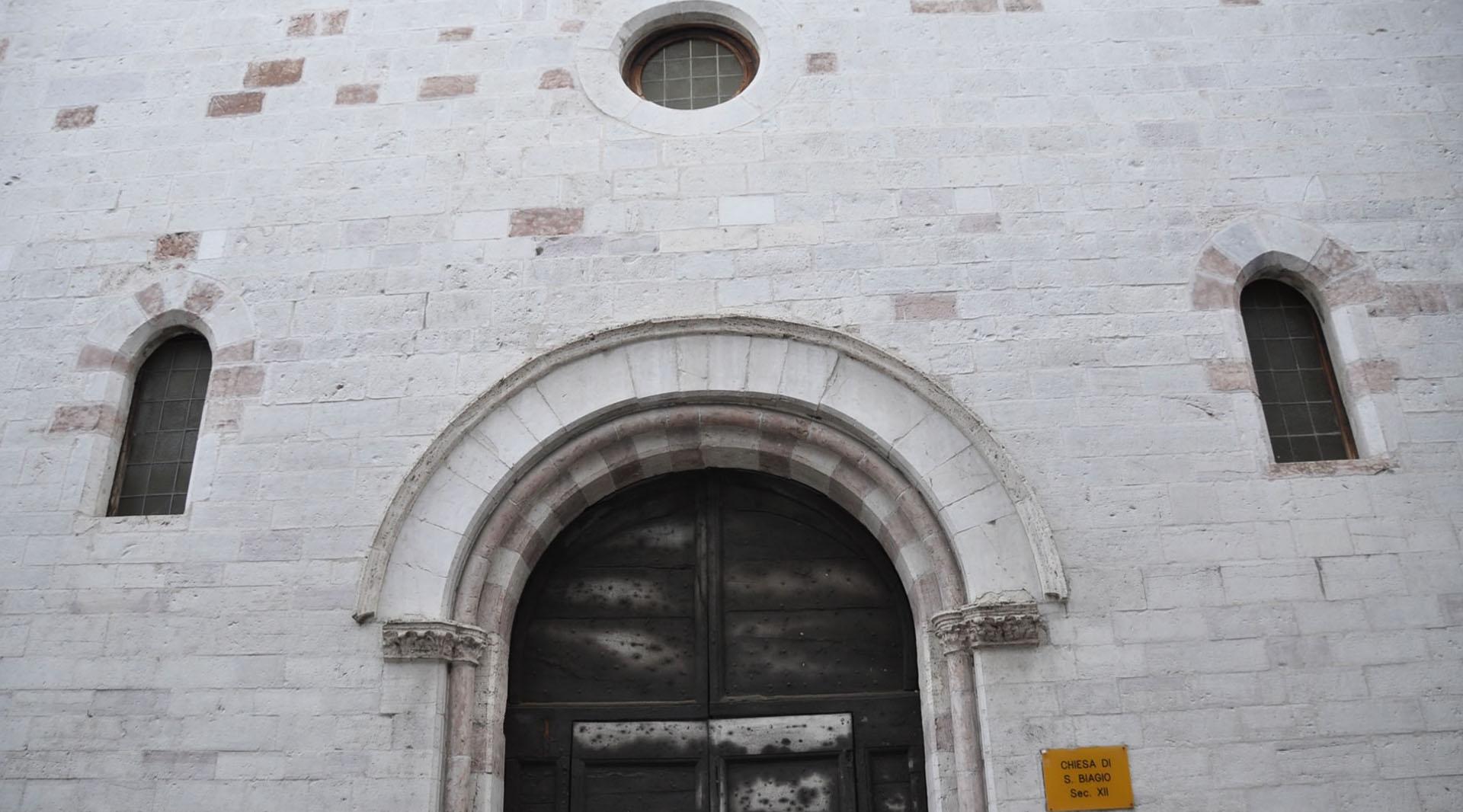 Façade en pierre de l’église San Biagio, avec un portail en arc, des fenêtres étroites et un oculus central.