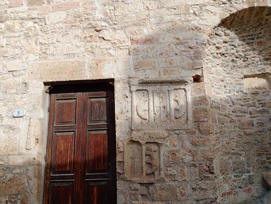 Porta in legno scuro incastonata in un muro di pietra con materiali di reimpiego e rilievi romani scolpiti.