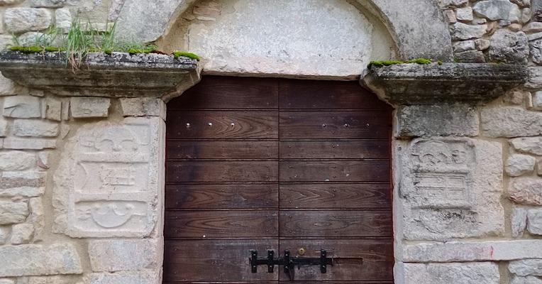 Portale di ingresso di chiesa in pietra, con murature che presentano materiali di riutilizzo del periodo romano