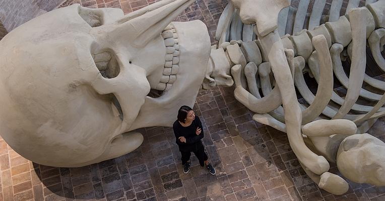 Giant skeleton installed in a deconsecrated church, surrounded by soft lighting and brick architecture