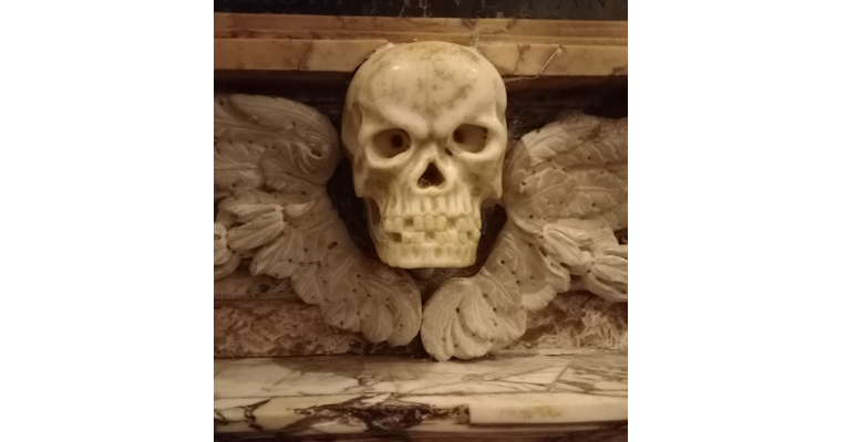 Teschio scolpito in marmo con ali decorative, parte di un monumento funebre