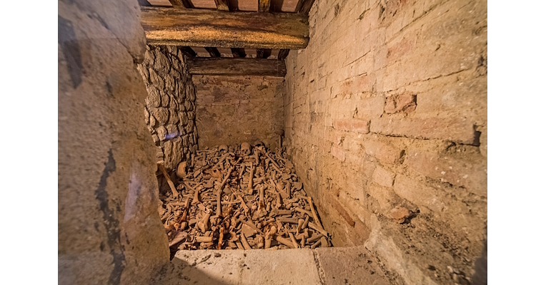 Stanza in pietra con soffitto in legno che contiene un accumulo di ossa e teschi umani