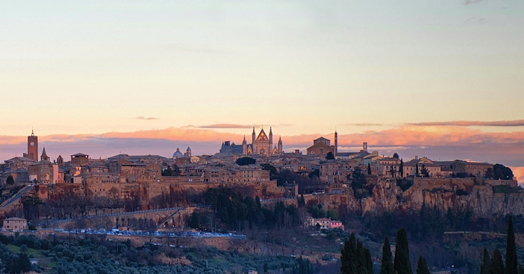 Vista panoramica della città di Orvieto illuminata dalla luce del tramonto, adagiata sulla sua rupe tufacea.