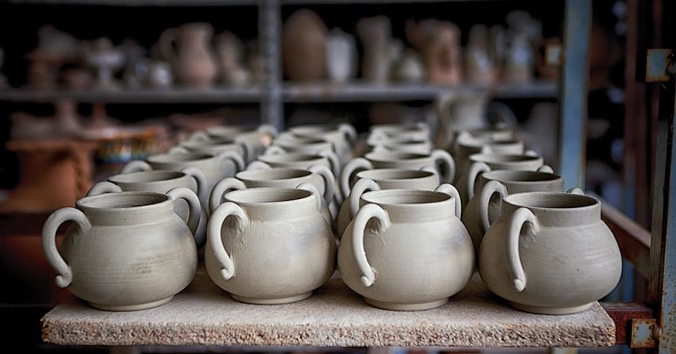 Rows of unglazed terracotta pots neatly arranged on a shelf in a pottery workshop.