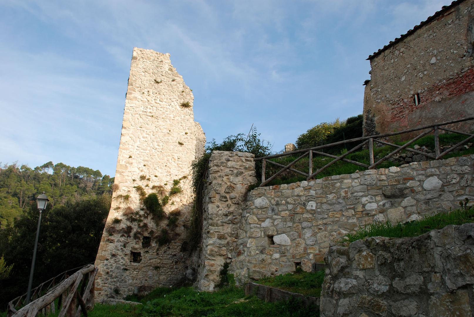 Ruins of the Castle of Poggio di Otricoli: remains of a stone tower among ancient walls, vegetation and clear sky.