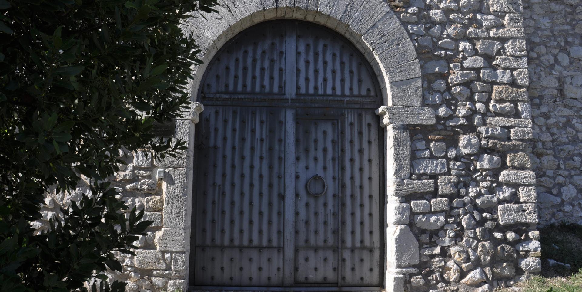 Reinforced wooden door with iron studs, framed by a stone arch on the walls of Castello del Poggio.