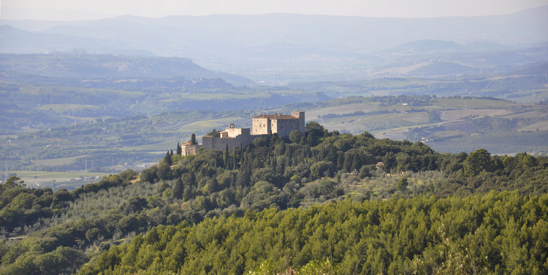 Panoramablick auf das Castello del Poggio, eingebettet ins Grün der umbrischen Hügel, mit Hügellandschaft im Hintergrund.
