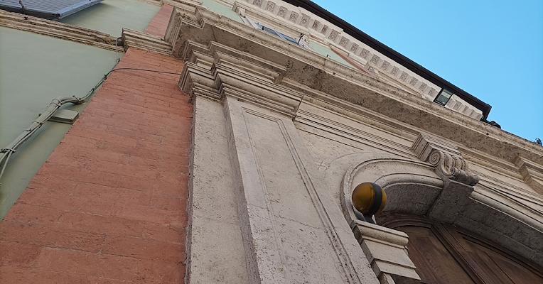 Vue en contre-plongée du portail monumental du Palazzo Conestabile Della Staffa, avec encadrements en pierre et façade historique.