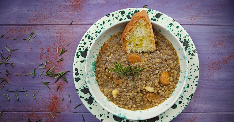 Soupe de lentilles avec carottes et pommes de terre, romarin et tranche de pain grillé sur assiette décorée, vue de dessus.