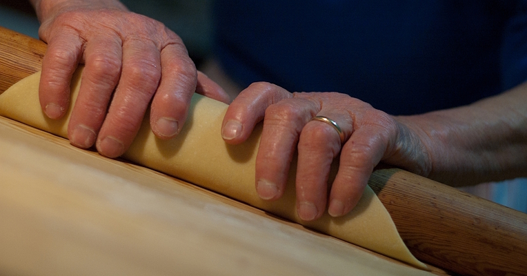 Mains étalant une feuille de pâte au rouleau sur une table en bois farinée.