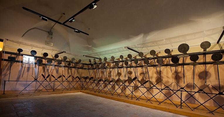Salle de musée avec une longue rangée de fers à gaufre en fer accrochés aux murs, éclairée doucement.