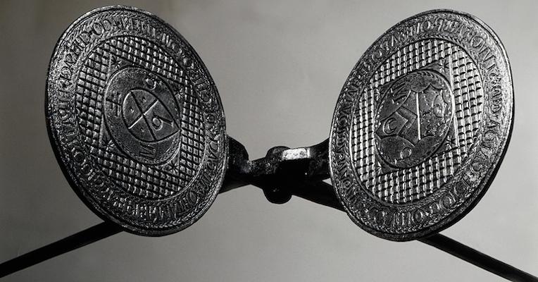 Gros plan d’un fer à gaufre avec plaques gravées et armoiries, sur fond neutre.