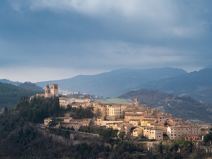 Veduta di Nocera Umbra arroccata su una collina, con il borgo e le torri medievali circondati da un paesaggio collinare.