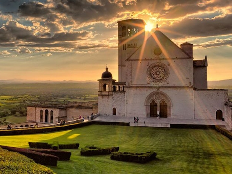 Veduta della Basilica di San Francesco ad Assisi illuminata dalla luce del tramonto.