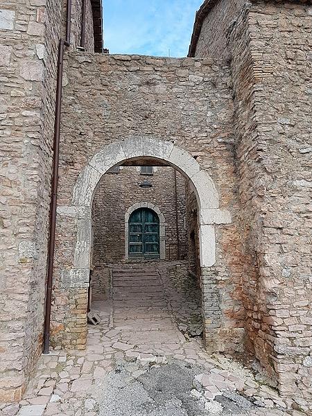 Arco in pietra all’ingresso del castello di Macerino, dal quale si scorge un con vicolo con scale e, in fondo, una porta verde