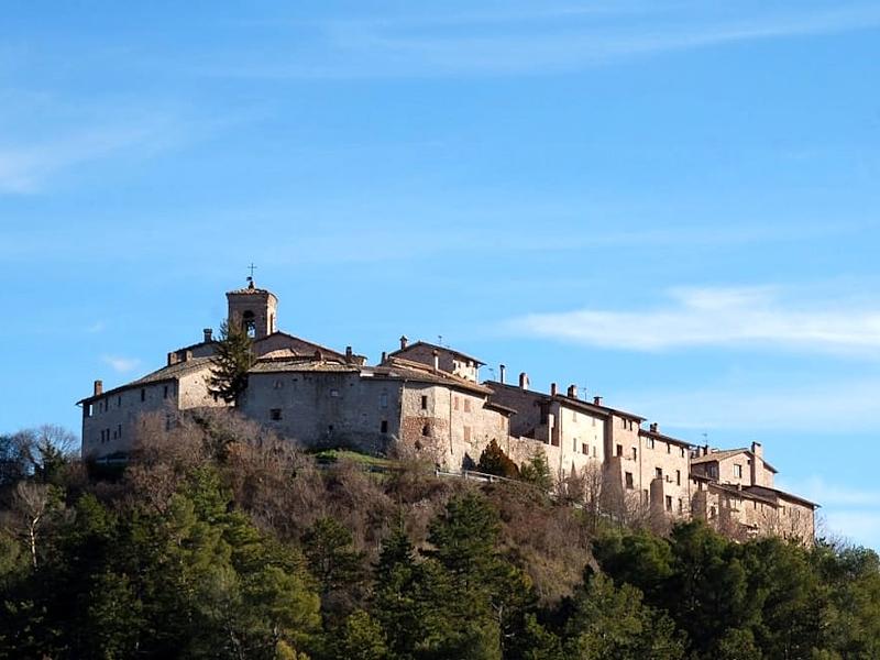 Vista dal basso del castello medievale di Macerino su una collina immerso nei boschi dei Monti Martani, con cielo limpido sullo sfondo