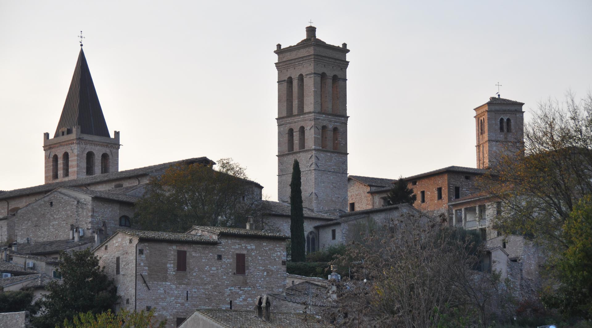 Panoramic view of the town of Spello at sunset, with the ancient historic center framed by bell towers rising among the houses.