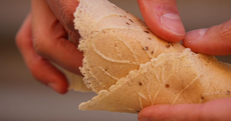 Hands holding a cone made from an artisanal wafer, with embossed patterns and anise seeds.