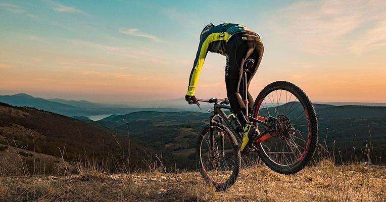 Mountain biker on a hill trail with a view of mountains at sunset.